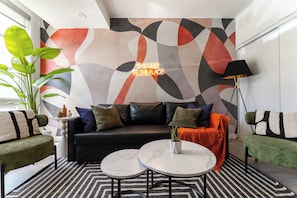 A modern living room with a black leather sofa, two round tables, and a geometric abstract wall design.