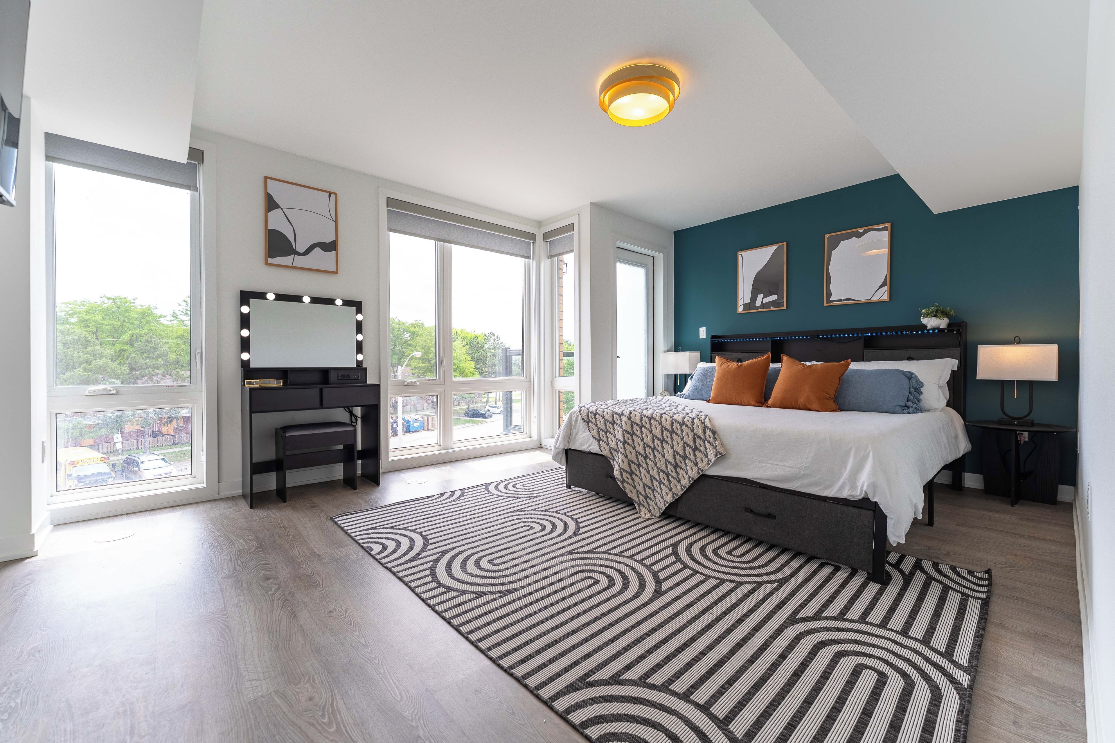 Une chambre moderne avec un grand lit, une coiffeuse avec éclairage, un bureau et une vue par la fenêtre.