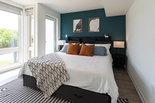 A modern bedroom with a large bed, bedside lamps, and a view of the outdoors.