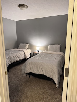 Quarto com duas camas, mesa de cabeceira, abajur e luminária no teto.