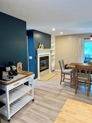 Uma sala de estar moderna com lareira, um espaço para café e uma sala de jantar com cadeiras e mesa de madeira.