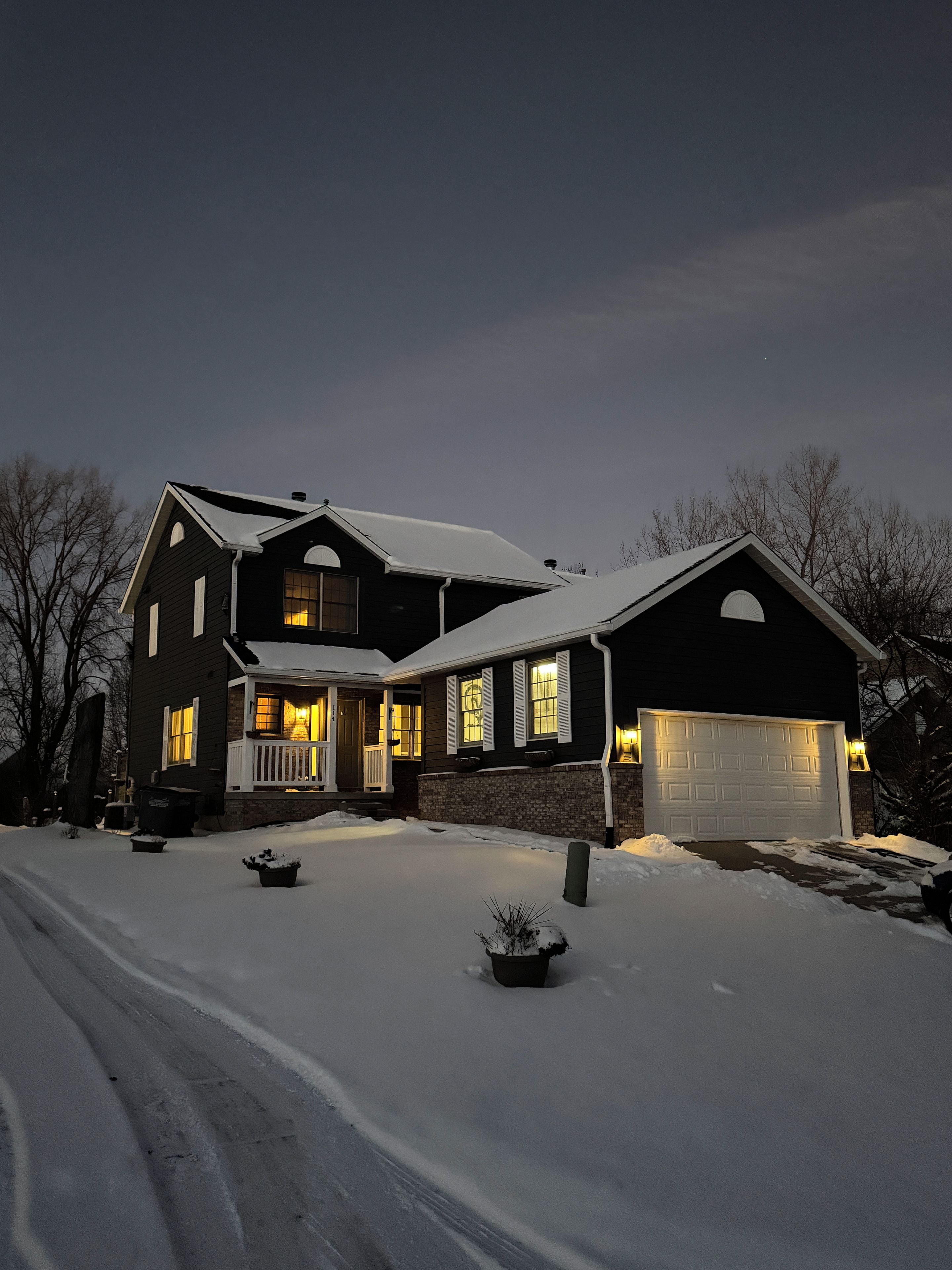 A two-story house with a garage, snow-covered driveway, and a front porch.
