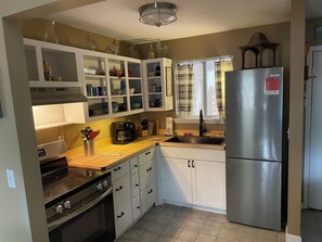 A kitchen with white cabinets, a stainless steel refrigerator, a stove, and a window with curtains. - Skye Villa is now available! Spacious  2 bedroom  in enchanting Fairfield Bay (Fairfield Bay)