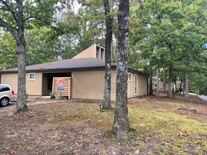 A single-story building with a garage, surrounded by trees and a driveway. - Skye Villa is now available! Spacious  2 bedroom  in enchanting Fairfield Bay (Fairfield Bay)