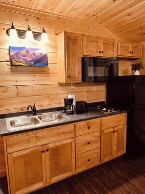 A kitchen with wooden cabinets, a stainless steel sink, a black refrigerator, and a coffee maker. - Cozy Mountain Cabin | Sleeps 6 | 11 Minutes to Sugarloaf | Minutes to Kingfield (Kingfield)
