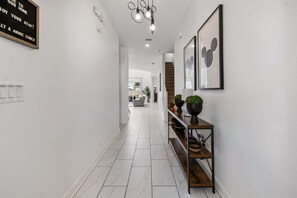 A hallway with a light switch panel, a framed sign, a staircase, and a console table with potted plants. - 6BR Championsgate Villa Near Disney! (Davenport)