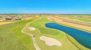 Vue aérienne d’un parcours de golf avec un obstacle d’eau, des bunkers de sable et une route qui longe le parcours.