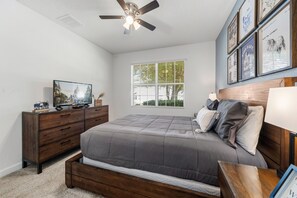A bedroom with a bed, a dresser, a ceiling fan, a window with blinds, and wall art. - 6BR Championsgate Villa Near Disney! (Davenport)