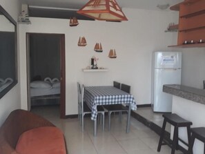 A compact living space with a dining table, chairs, a sofa, a refrigerator, and a kitchen counter. - BlackPoint (BALLENITA)