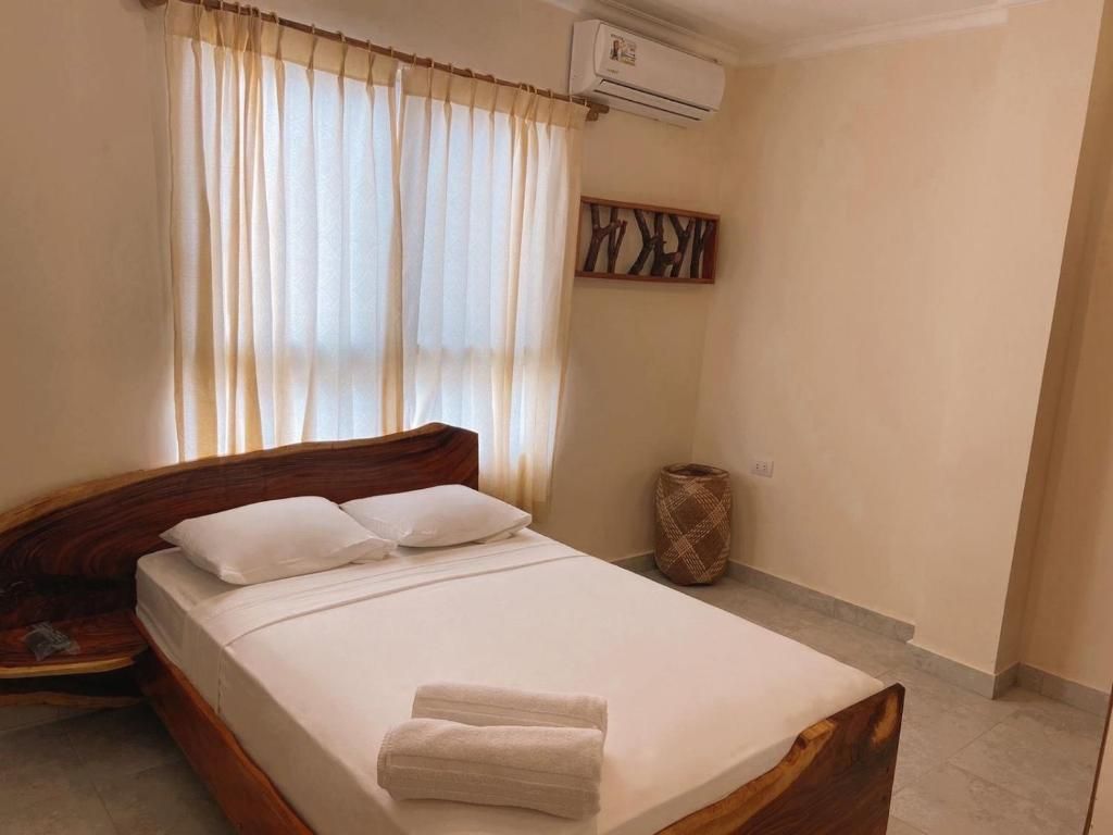 Una cama bien hecha con sábanas blancas y una toalla doblada, un cabecero de madera, un aire acondicionado de pared y un adorno mural.