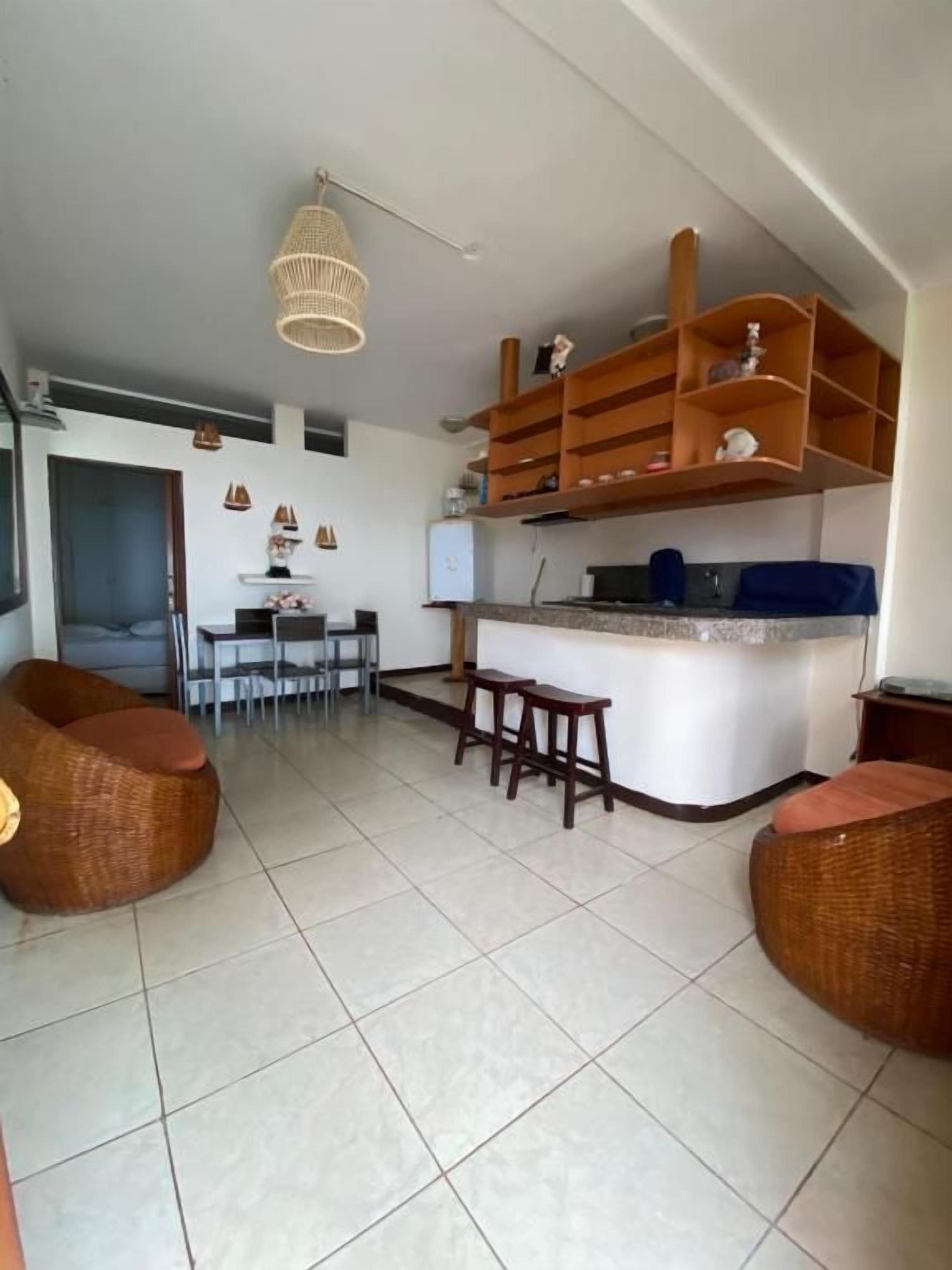 Amplia sala de estar con cocina, mesa de comedor y dos sofás de mimbre.