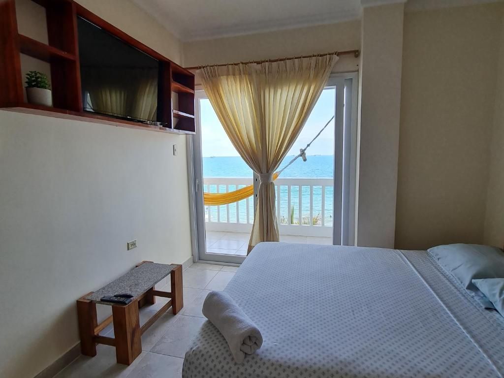 Un dormitorio con cama, un banco, una ventana con cortinas y vista al mar.