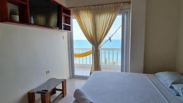 Un dormitorio con cama, un banco, una ventana con cortinas y vista al mar.