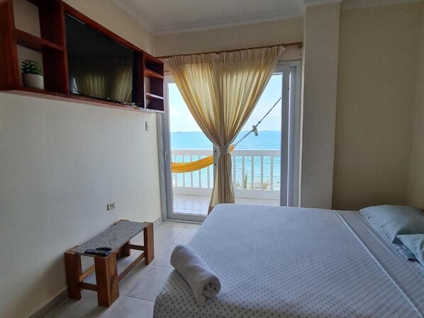 A bedroom with a bed, a bench, a window with curtains, and a view of the sea.