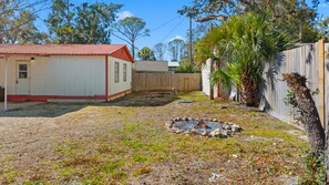 A backyard with a small fire pit, a wooden fence, and a house with a red roof. - The Red Roof River Cottage - Home in Steinhatchee (Steinhatchee)