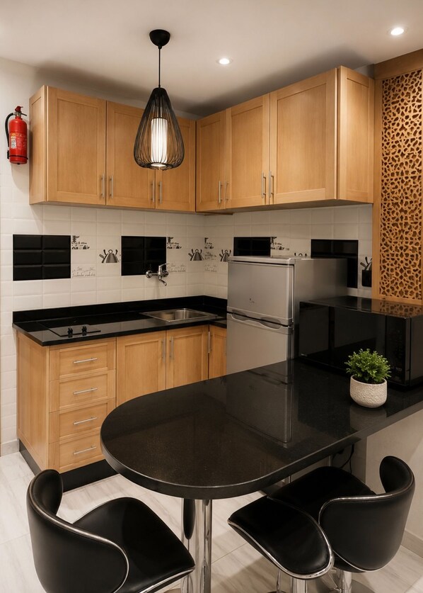 A modern kitchen with wooden cabinets, a black countertop, stainless steel appliances, and a round dining table with black chairs. - Modern 1BR in Hassan / AC & Fast Wi-Fi (Rabat)