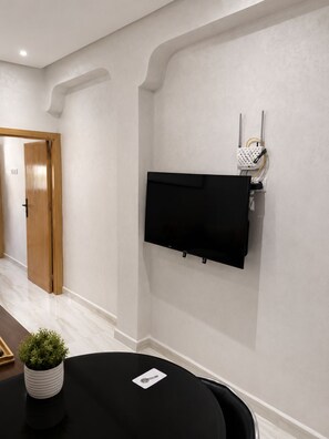 A conference room with a flat-screen TV mounted on the wall, a potted plant on the table, and a door leading to another room. - Modern 1BR in Hassan / AC & Fast Wi-Fi (Rabat)