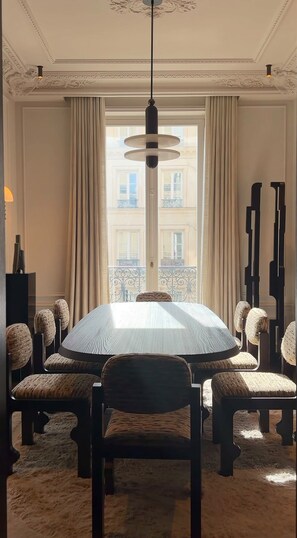 Een eetkamer met een ronde tafel, stoelen en een hanglamp.