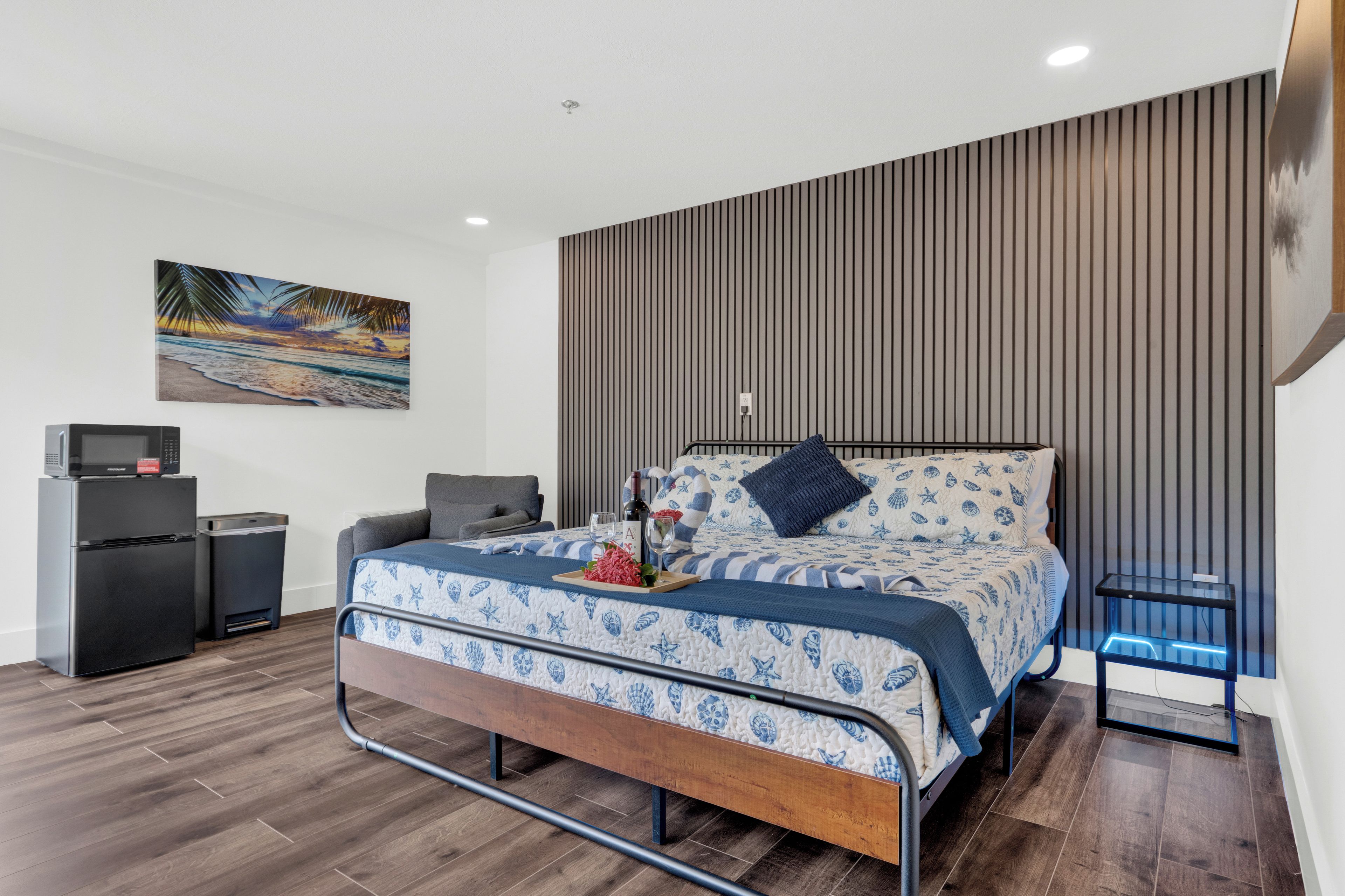 A modern bedroom with a bed, a small desk, a refrigerator, and a wall-mounted TV.