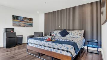 A modern bedroom with a bed, a small desk, a refrigerator, and a wall-mounted TV.
