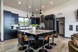 A modern kitchen with a central island, bar stools, and pendant lighting. - NEW! Hillside Home w/Hot Tub, Mountain Views, EV Charging (Williams)