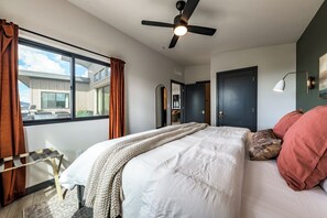 A bedroom with a bed, a ceiling fan, a window with curtains, a door, and a lamp. - NEW! Hillside Home w/Hot Tub, Mountain Views, EV Charging (Williams)
