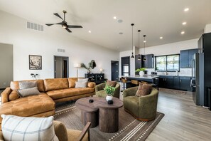 A modern living room with a brown leather sofa, green armchairs, and a wooden coffee table. - NEW! Hillside Home w/Hot Tub, Mountain Views, EV Charging (Williams)