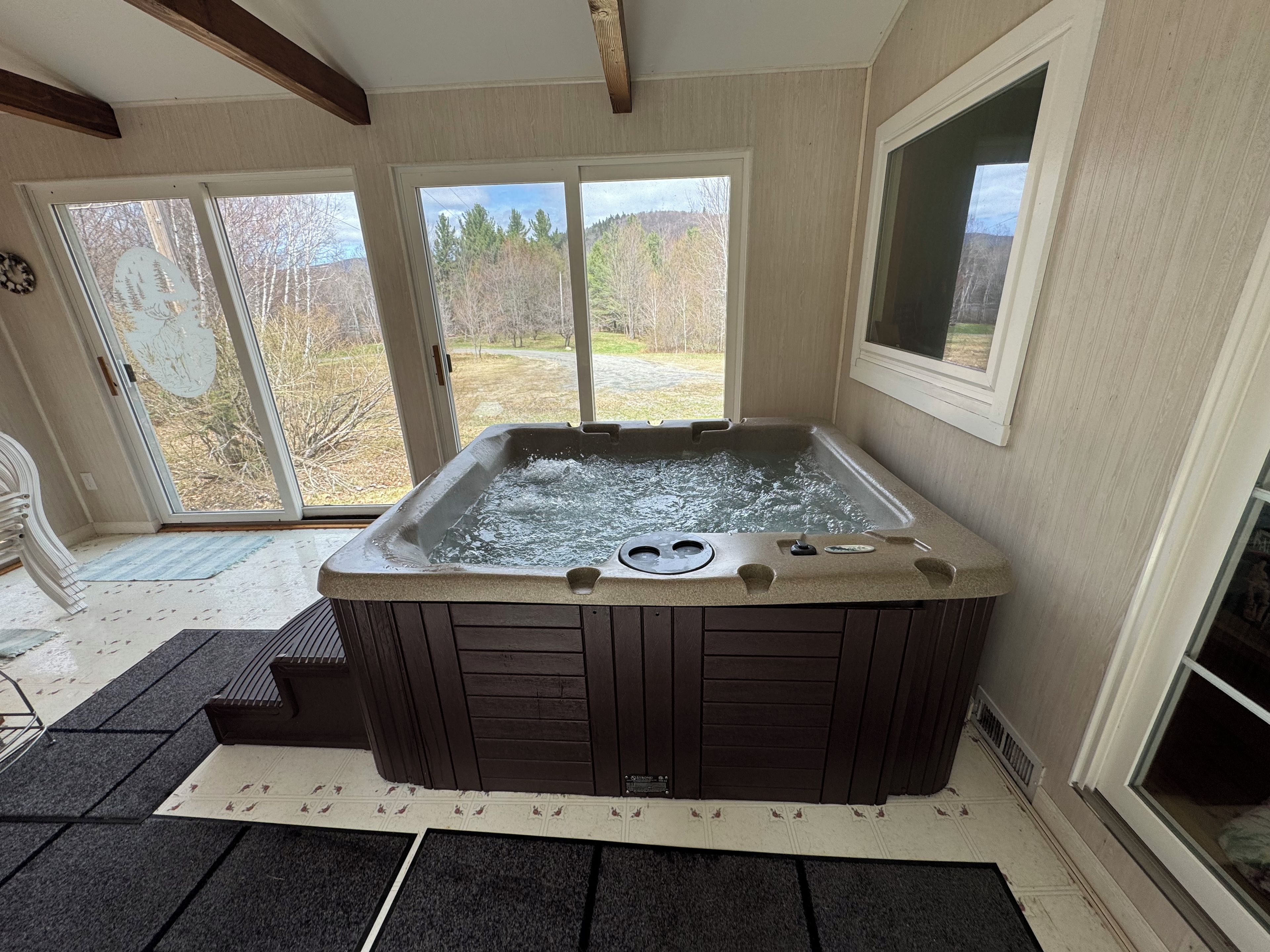 A hot tub in a room with large windows, a door, and a wooden ceiling.