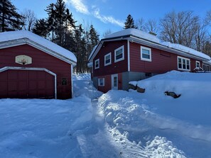 A red building with a garage and a second-story structure, surrounded by snow and trees. - Cozy Ski Mountain House (Wardsboro)