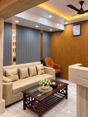 A modern living room with a sofa, a coffee table, and a reception desk. - Hotel Tatva Kashi (Varanasi)