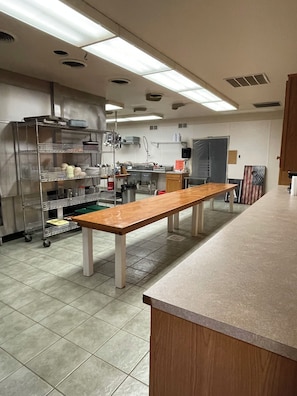 Una cocina amplia con una larga mesa de madera, electrodomésticos de acero inoxidable y piso de baldosas.
