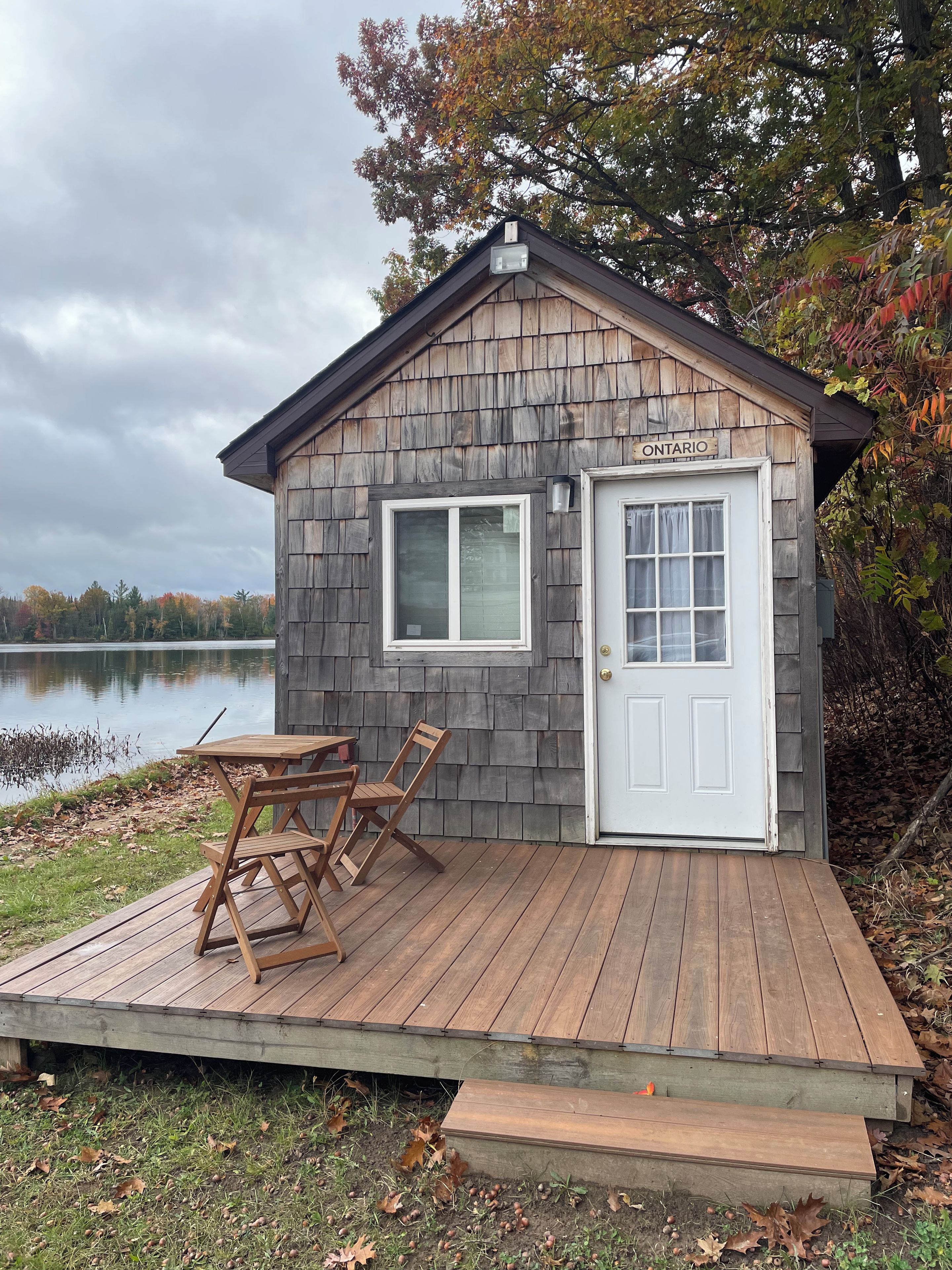 A small wooden cabin with a dock, a table, and chairs, located near a lake.
