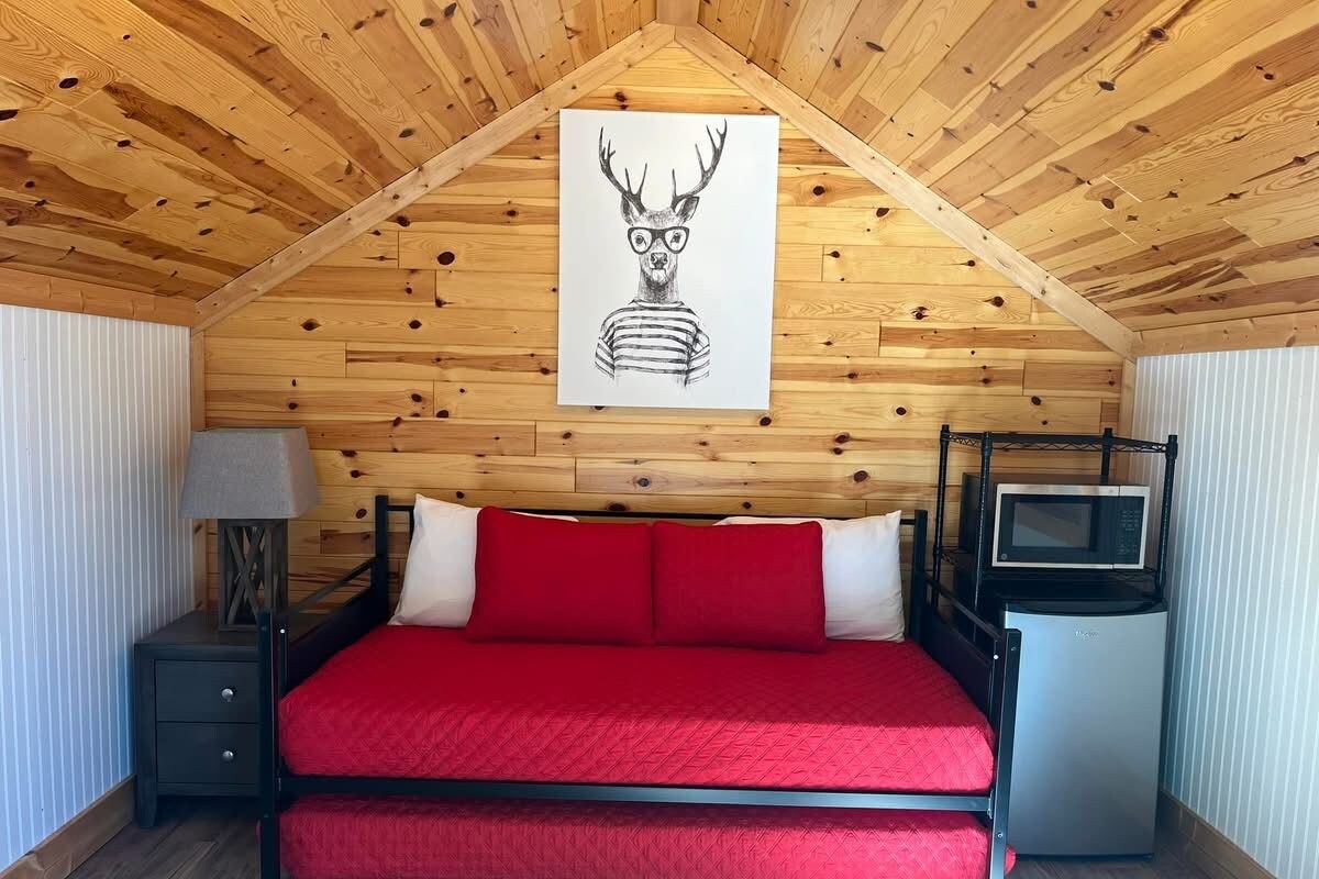 Una habitación con cama, mesita de noche, lámpara, microondas y un cartel en la pared.