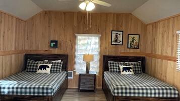 A room with two wooden beds, a ceiling fan, a window with blinds, and a wall-mounted light fixture.