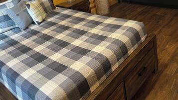 Ein Zimmer mit einer Holzwand, einem Bett mit kariertem Überwurf, einer Nachttischlampe, einer schwarzen Couch mit einem Bärenkissen und einem Korbwäscher.