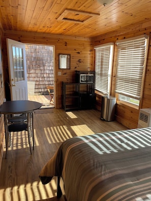 A wooden cabin interior with a bed, a table, and a bench.