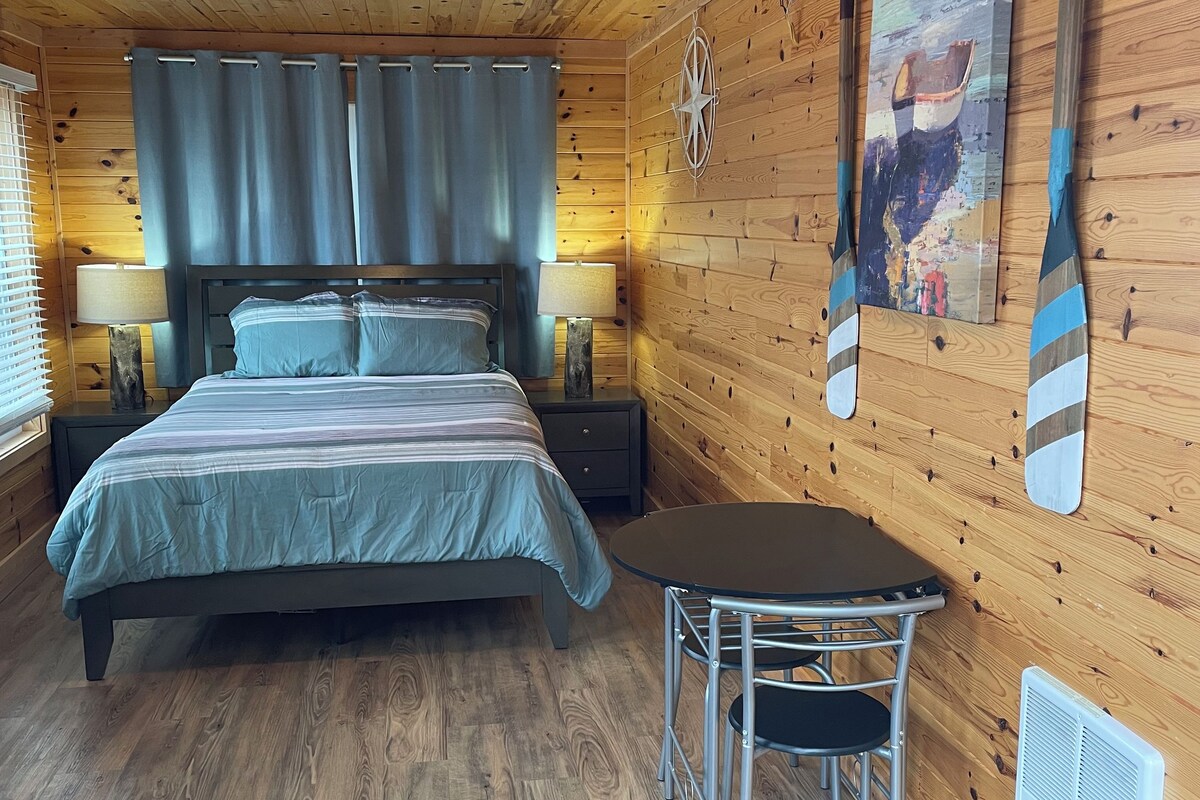 Habitación con paneles de madera, una cama, una mesa y una obra de arte colgada en la pared.