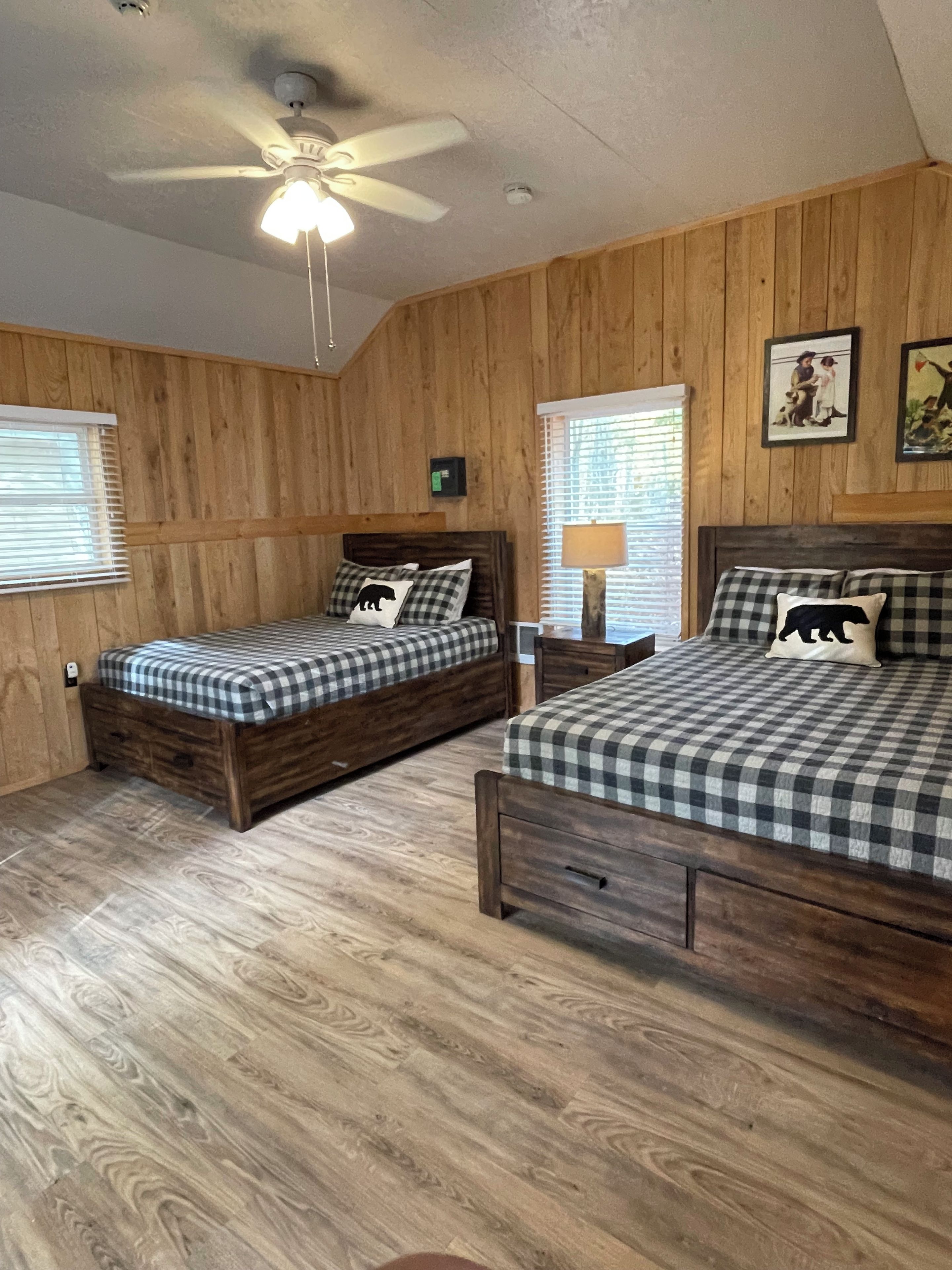 Un dormitorio con dos camas de madera, un ventilador de techo y paredes de madera.