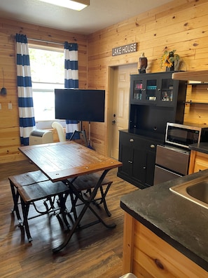 A wooden interior with a dining table, black cabinets, a microwave, and a sign reading 'LAKE HOUSE'.