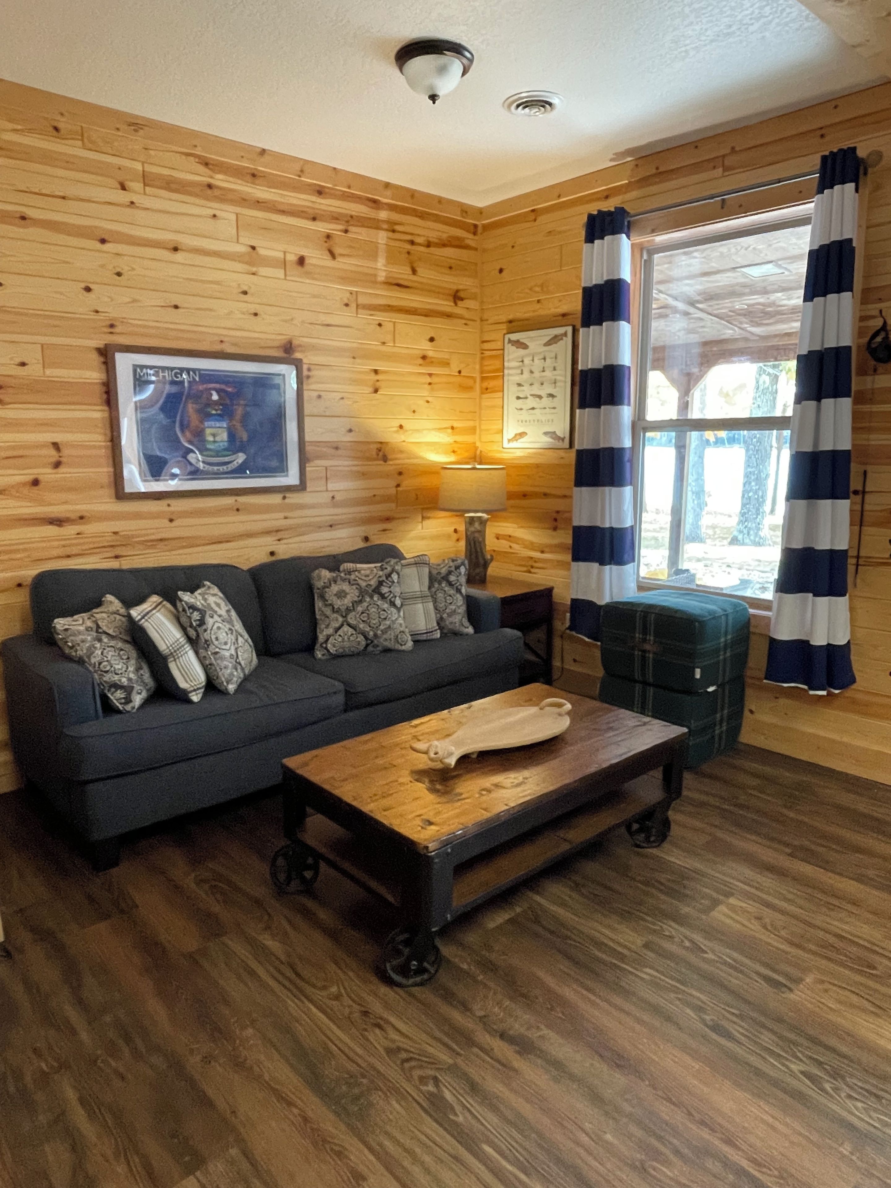 A cozy room with a wooden wall, a sofa with patterned cushions, a small table, and a window with curtains.