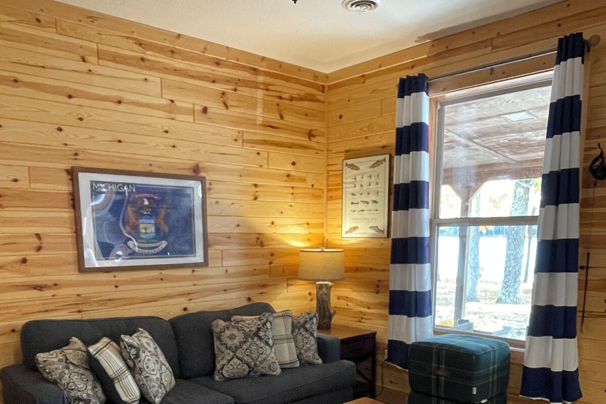 Una habitación acogedora con pared de madera, un sofá con cojines estampados, una mesita y una ventana con cortinas.