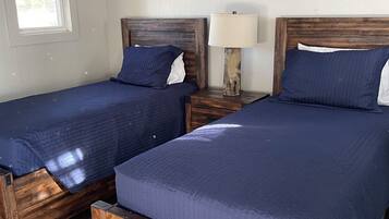 A bedroom with two wooden beds, a nightstand with a lamp, a painting on the wall, and a window.