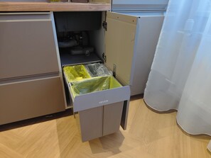 Eine Küche mit einer Schublade, die zwei Behälter enthält, einen gelben und einen grauen, sowie ein Kühlschrank.