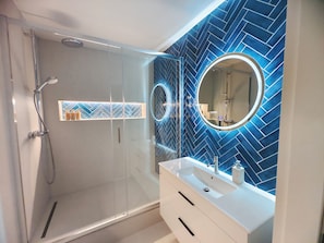 Un baño moderno con cabina de ducha de vidrio, tocador blanco con espejo y salpicadero de azulejos en patrón de espiga azul.