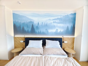 Un dormitorio con una cama, dos mesitas de noche y un amplio mural en la pared que representa un paisaje boscoso.