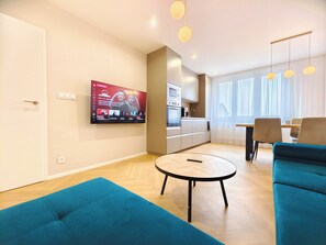 Ein modernes Wohnzimmer mit einem wandmontierten Flachbildfernseher, einem runden Couchtisch und einem blauen Sofa.