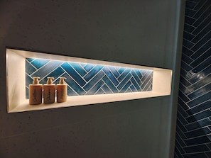 Un baño con estante empotrado que exhibe tres botellas de artículos de aseo.