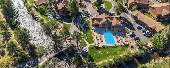 An aerial view of a residential area with a large swimming pool surrounded by houses, a bridge, and a river.