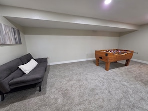 Ein Zimmer mit einem grauen Sofa, einem Holztischkicker und einem grauen Teppich.