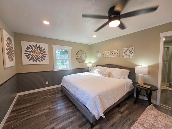 A bedroom with a bed, a ceiling fan, wall art, and a window.